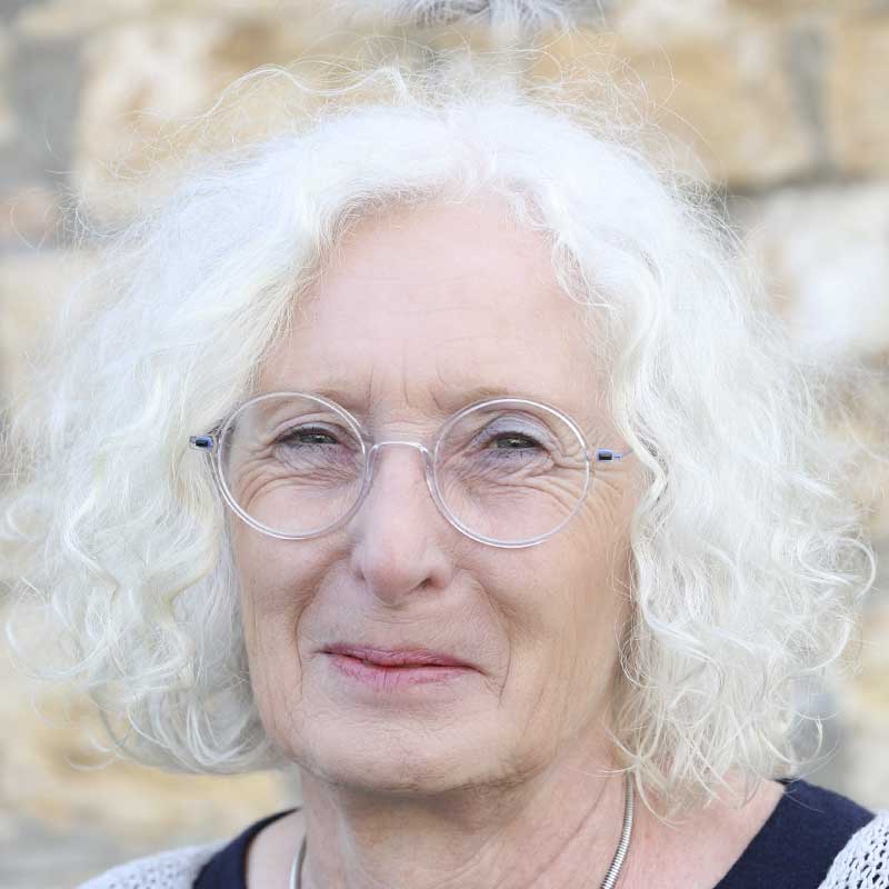 Eine ältere Dame mit weißen Haaren und Brille lächelt.