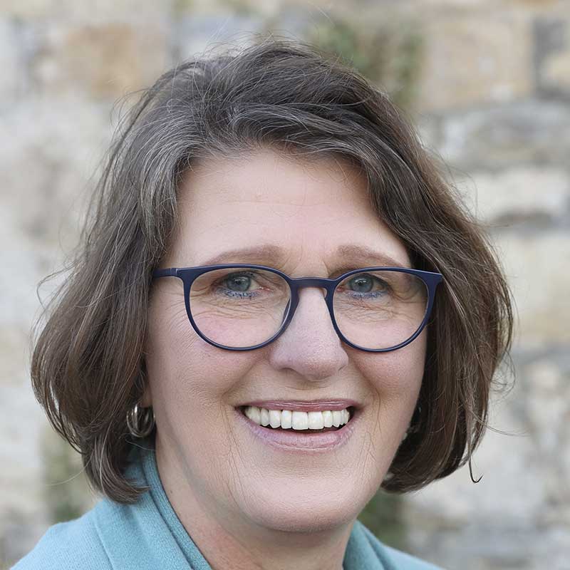 Eine Frau mit kurzen braunen Haaren und Brille lächelt.