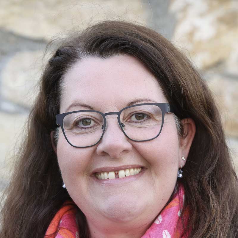 Eine Frau mit langen braunen Haaren, Brille und einem freundlichen Lächeln.